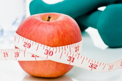 Measuring tape wrapped around a red apple with weights in the background