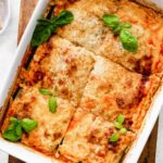 A square baking dish with tofu lasagna made with zucchini noodles cut into squares and garnished with fresh basil.