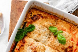 A square baking dish with tofu lasagna made with zucchini noodles cut into squares and garnished with fresh basil.