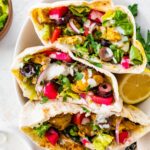 Three halves of chicken shawarma pita pockets stacked in a bowl, filled with veggies, olives, pickled turnips, and topped with yogurt sauce and fresh parsley.